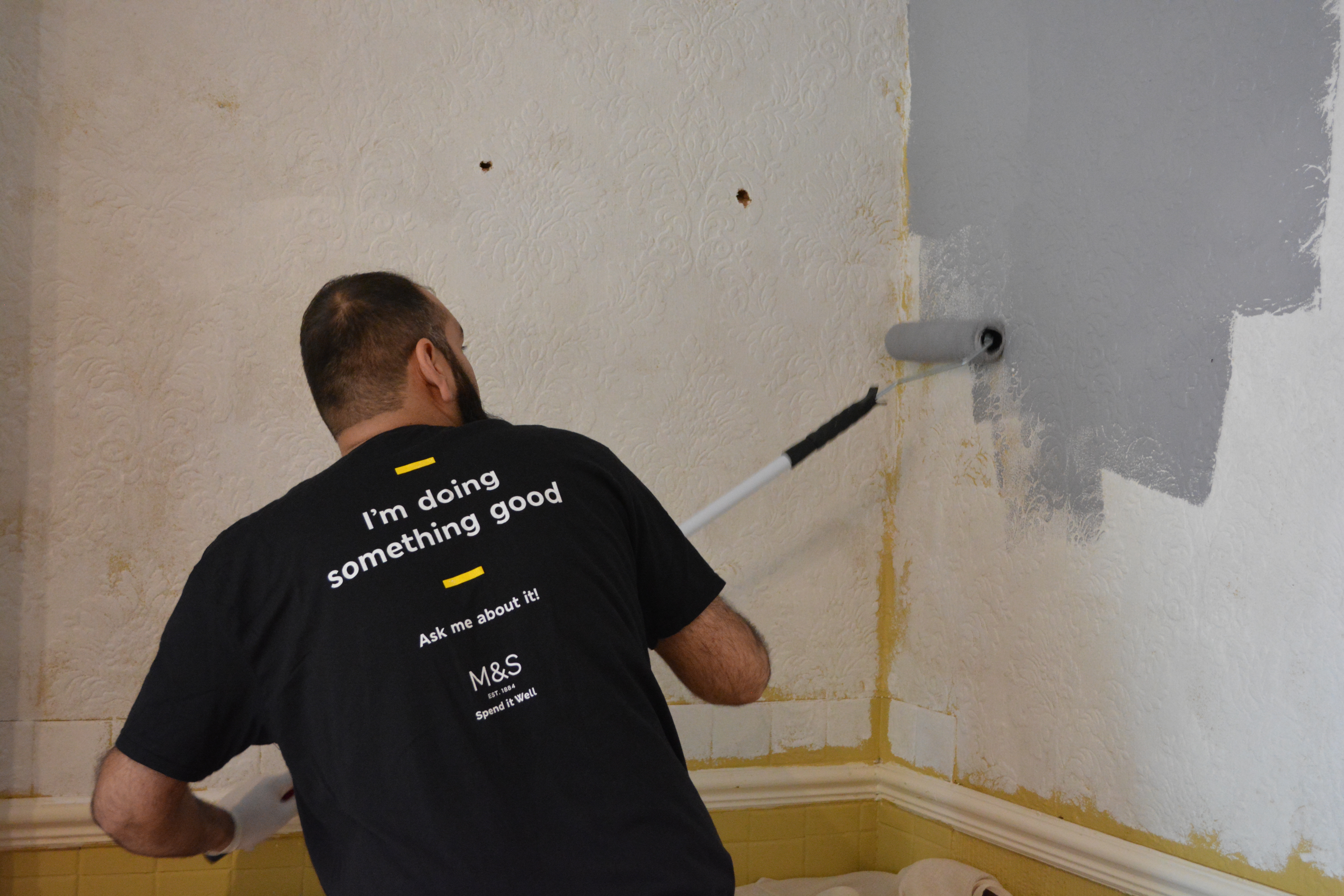 Paint volunteer redecorating a room in light grey paint.