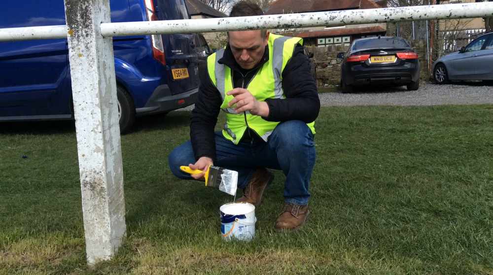 A volunteer painting a fence at Clayton Rugby Club with recycled and cheap paint from Community RePaint Bradford.