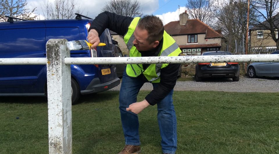 A volunteer painting a fence at Clayton Rugby Club on their community action day with recycled and cheap paint from Community RePaint Bradford.