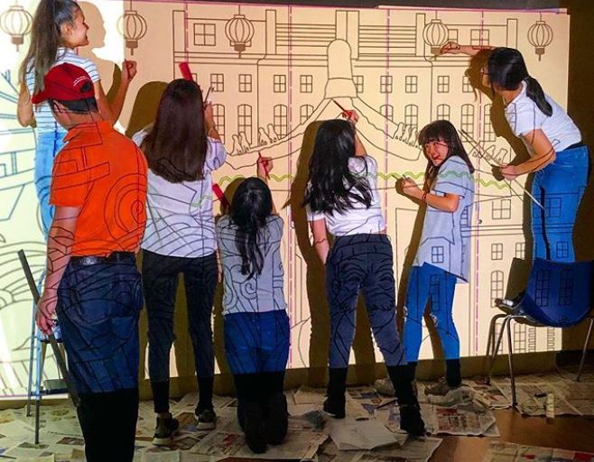 Members of the London Chinese Community Centre painting a mural using cheap and reusable paint from Regis Road Household Waste Recycling Centre.