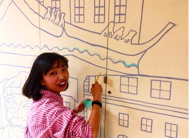 A member of the London Chinese Community Centre painting a mural using cheap and reusable paint from Regis Road Household Waste Recycling Centre.