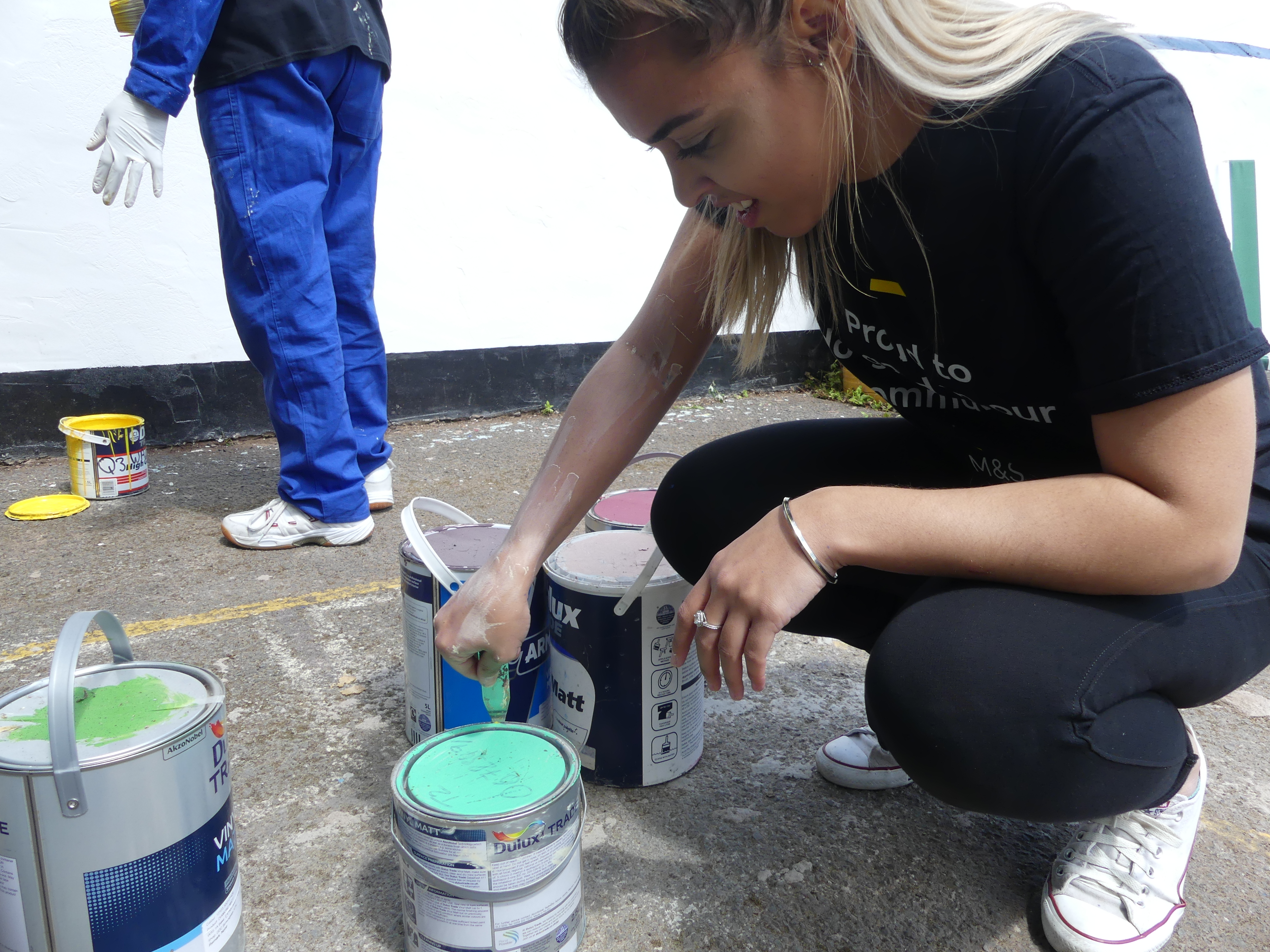 A volunteer opening a green paint container in preparation of painting a community mural using cheap and recycled paint from Community RePaint Birmingham.