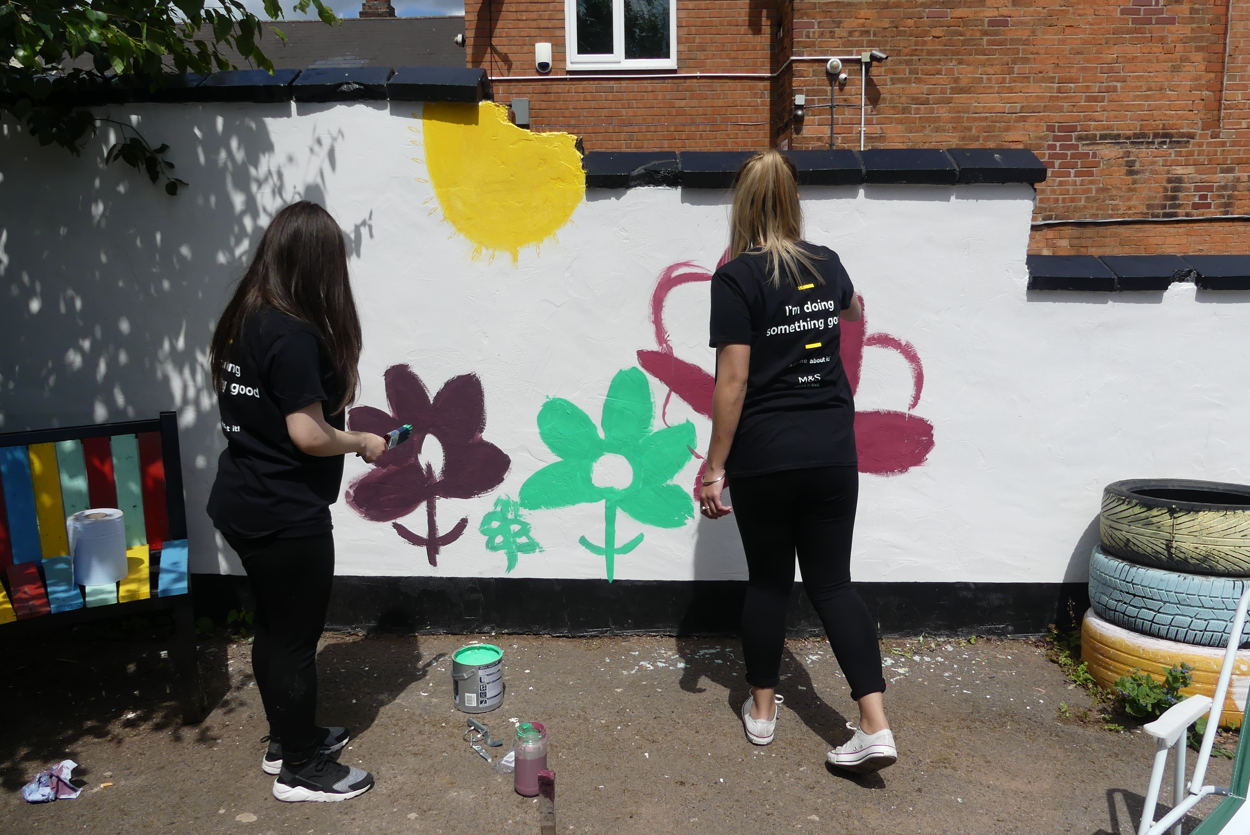 Volunteers painting a community mural using cheap and recycled paint from Community RePaint Birmingham. The mural is of flowers and insects on a white background.