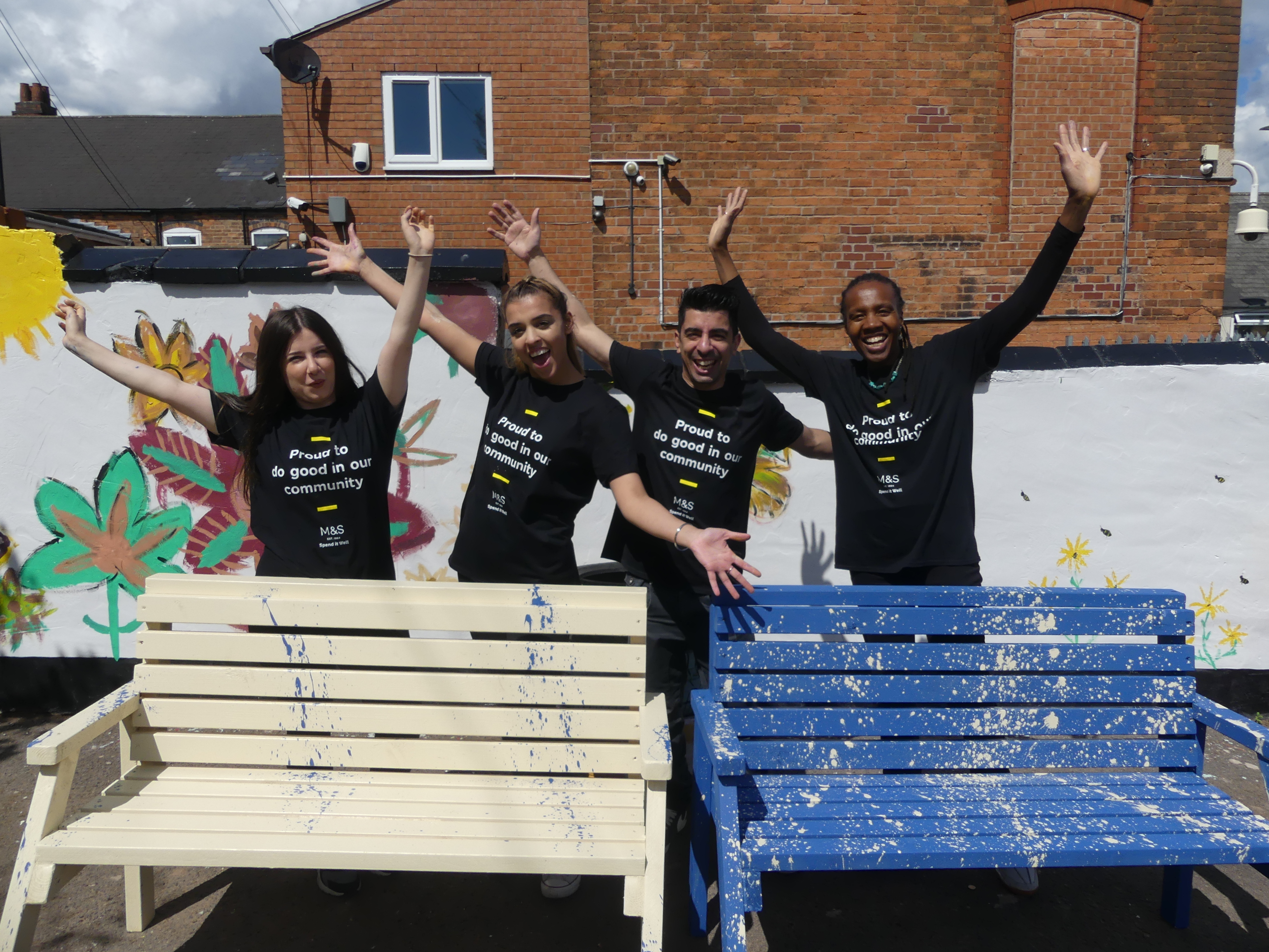 Volunteers posing in front of a newly painted a community mural and benches using cheap and recycled paint from Community RePaint Birmingham. The mural is of flowers and insects on a white background.