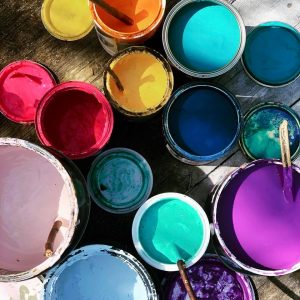 Looking into a variety of paint containers with their lids removed. There is a selection of colours including, pink paint, yellow paint, blue paint, turquoise paint, purple paint and orange paint.