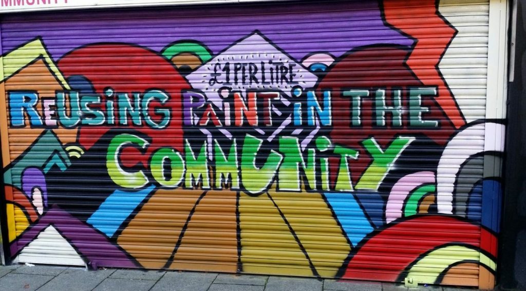 The shuttered entrance of Community RePaint Hull and East Riding. The shutter has been painted in bright colours using paint from the scheme and reads: £1 per litre. Reusing Paint in the Community.