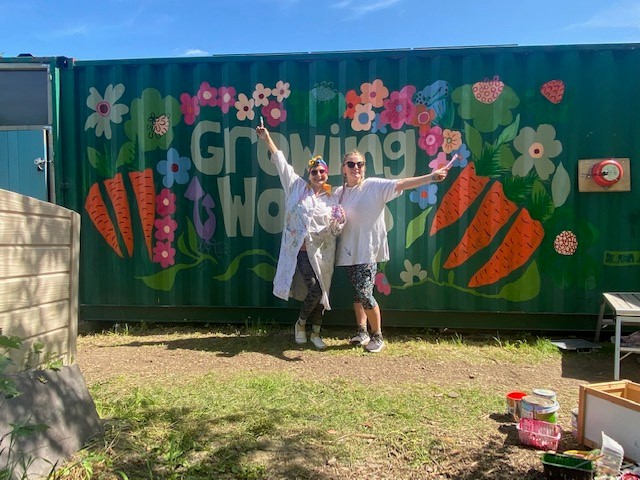 Artist, Safrana Art, and a volunteer in front of the finished allotment mural using leftover paint from Community RePaint Bradford